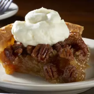 Traditional Texas Pecan Pie topped with fresh whipped cream.